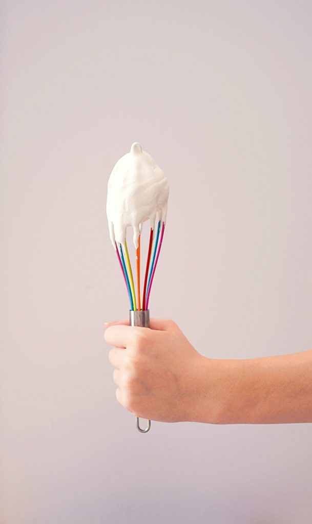 Ein bunter Schneebesen, auf dem etwas geschlagenes Eiweis ist.